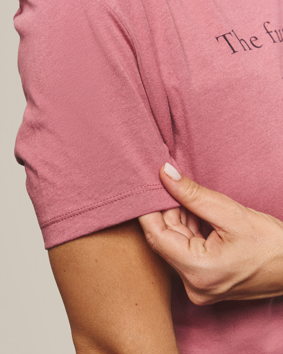 Close-up of the cotton and sleeve hem of the Future Tee in Mauve, pinched between finger and thumb.