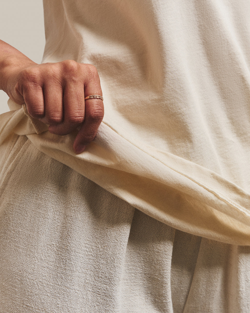 Close-up of the soft cotton and hem of the Still Tee in Warm Ivory, held between finger and thumb.