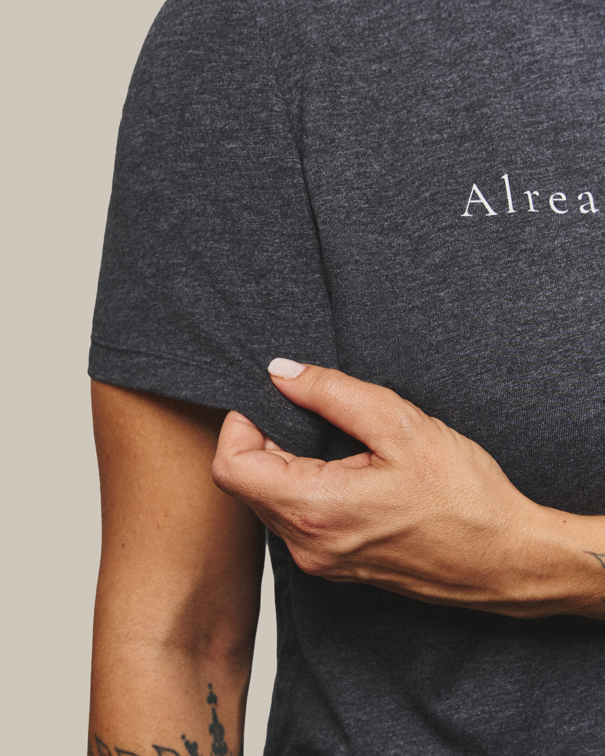 Close-up of the short sleeve and the heather cotton-blend fabric of the Strength Tee, pinched between finger and thumb.